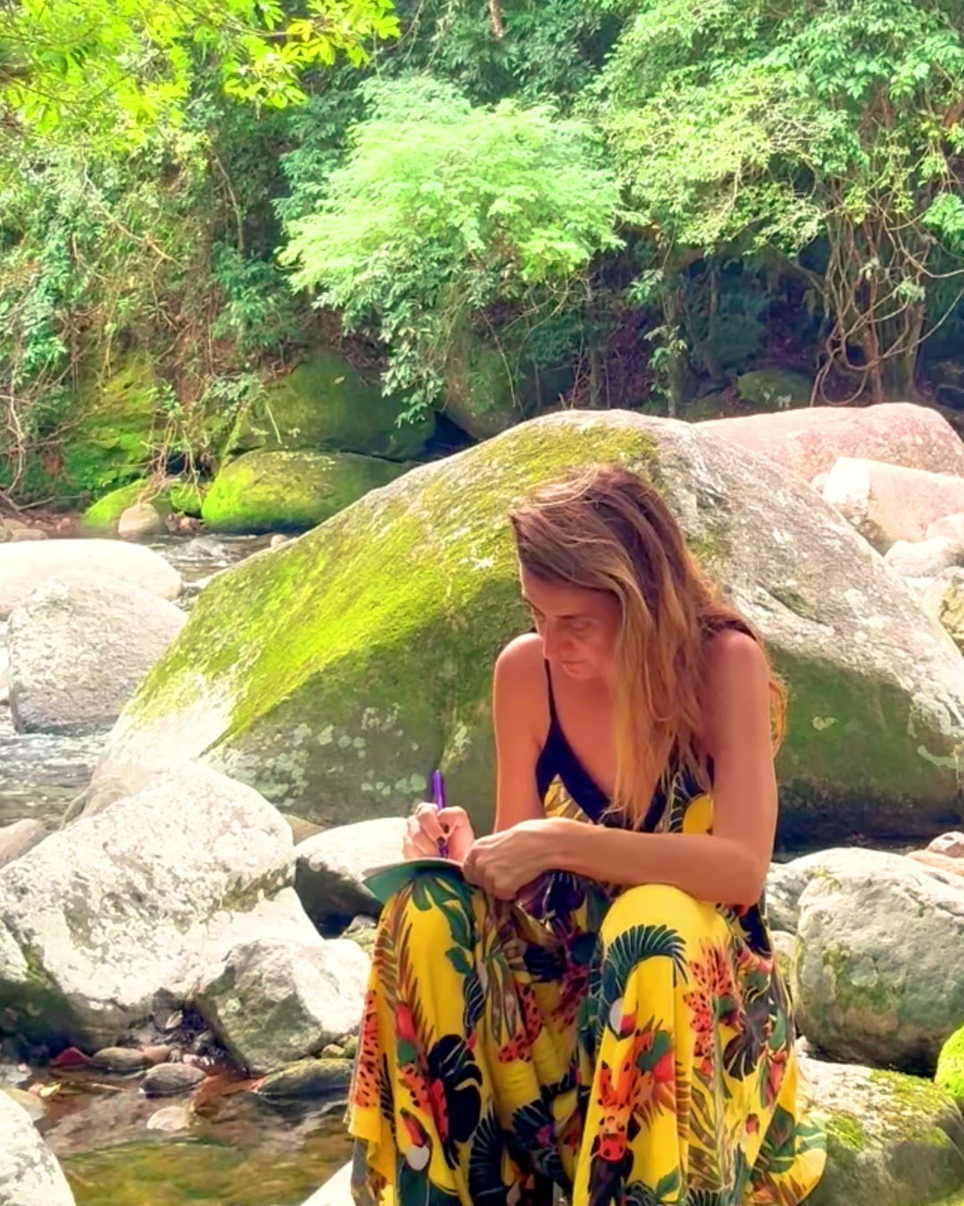 Danielle sitting on a river rock, writing in a notebook